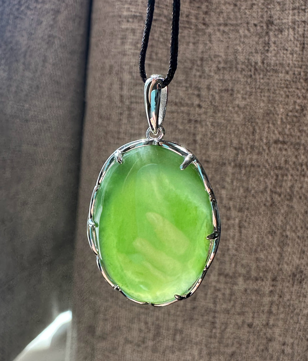 Oval green jade pendant in a silver bezel on a black cord necklace