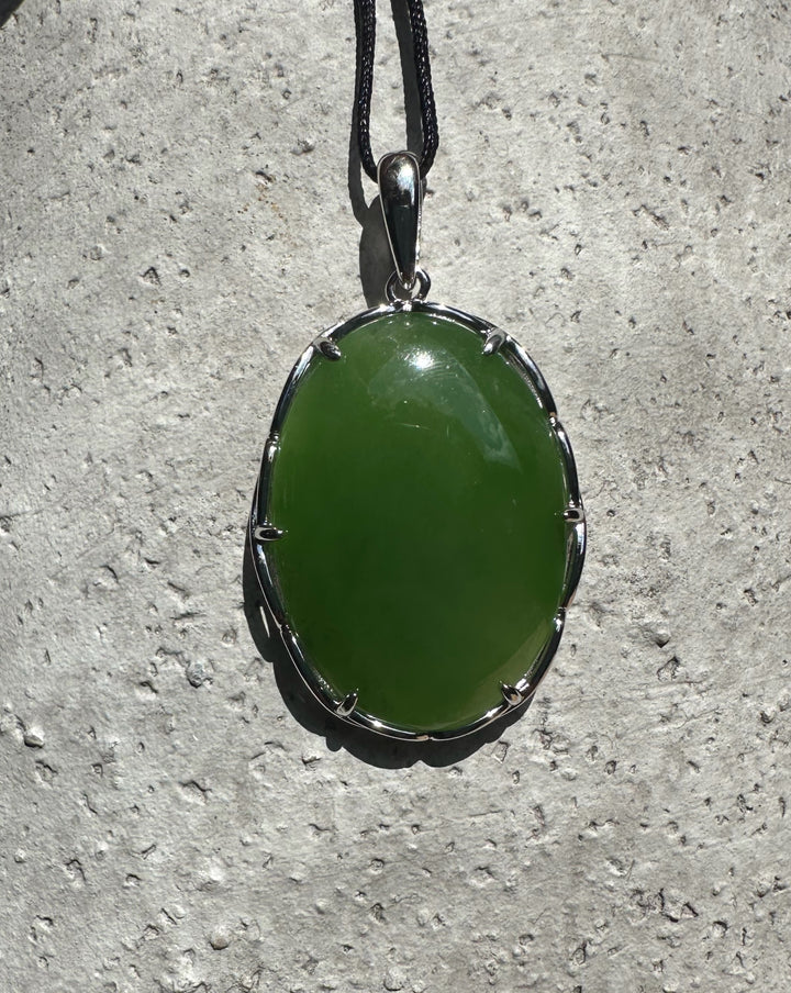 Green jade pendant in a silver bezel with a bail on a black cord against a concrete surface