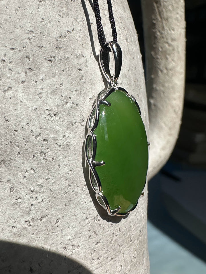 Side view of a green jade pendant in a silver frame hanging from a black cord