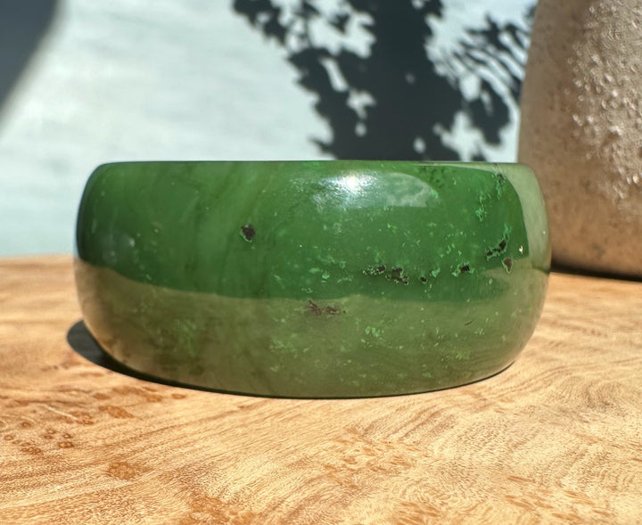 Wide Cassiar jade bangle with a light tan stripe across the middle and bright green hue.