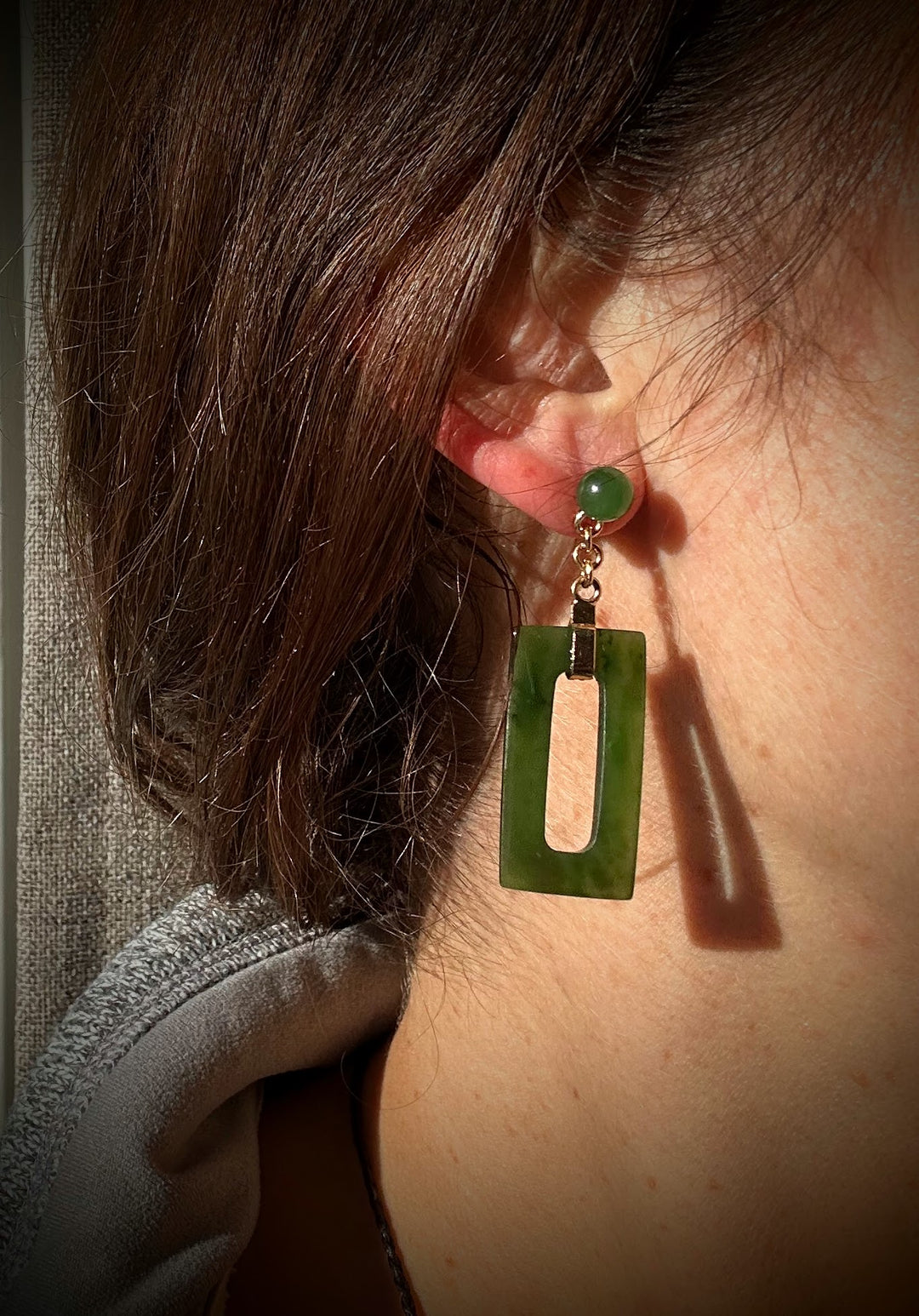 Model wears jade green rectangle drop earring with round stud and gold bail.
