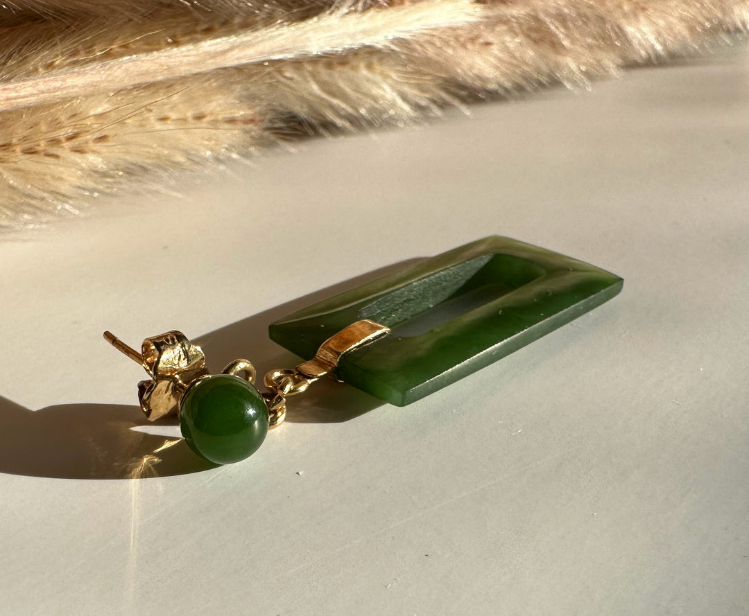 Close up of jade rectangle drop earring showing round green top bead and hollow rectangular pendant with gold bail.