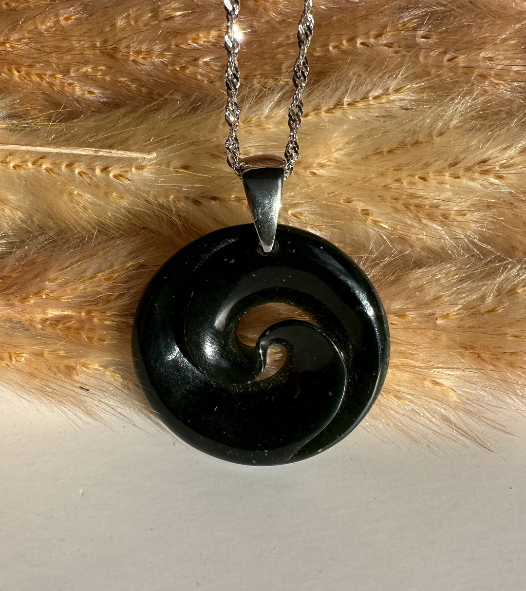 Polished black nephrite jade koru pendant with a spiral cutout on a silver chain