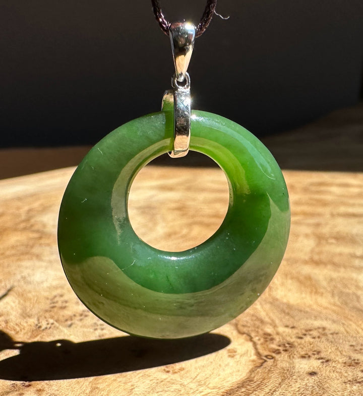 Green jade pendant with silver ring on a wooden surface