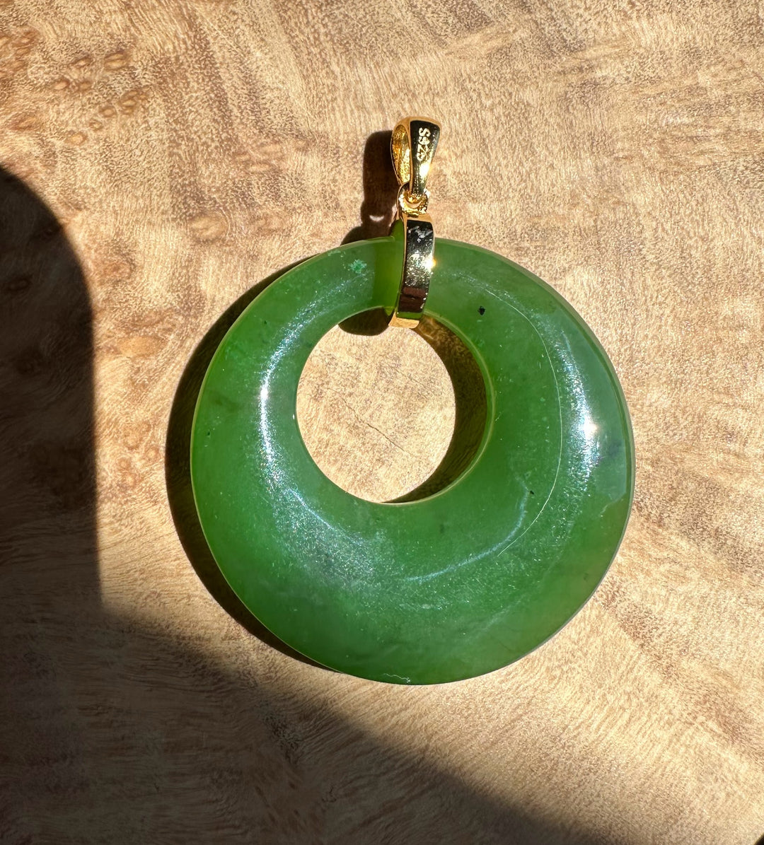 Green jade pendant with gold chain on a wooden surface