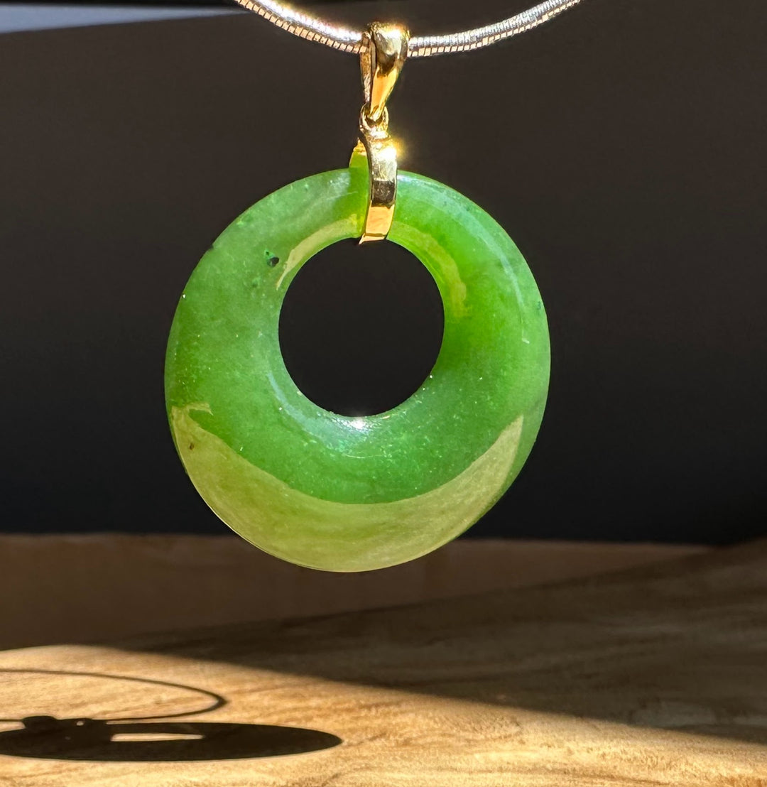 Green jade pendant on a chain against a dark background