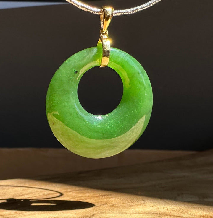 Green jade pendant on a chain against a dark background