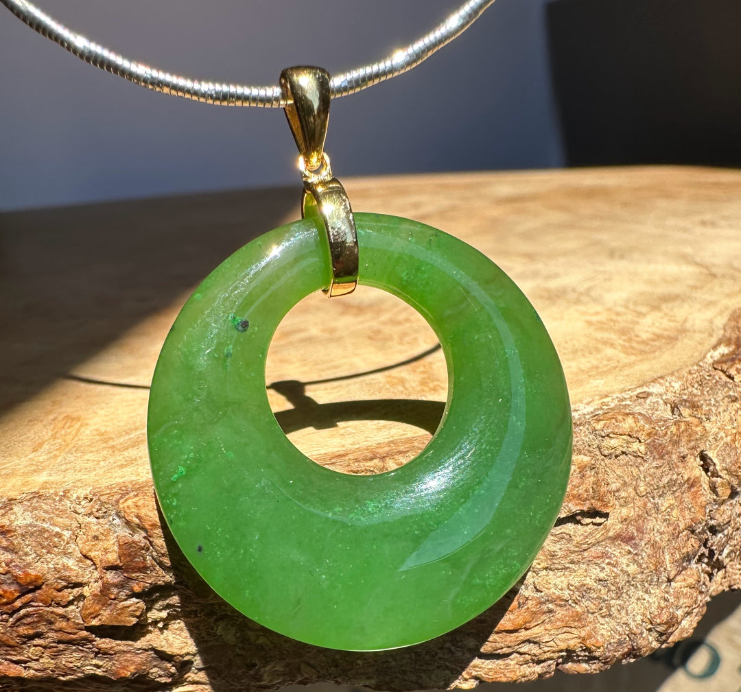 Green jade pendant with gold accent on a wooden surface