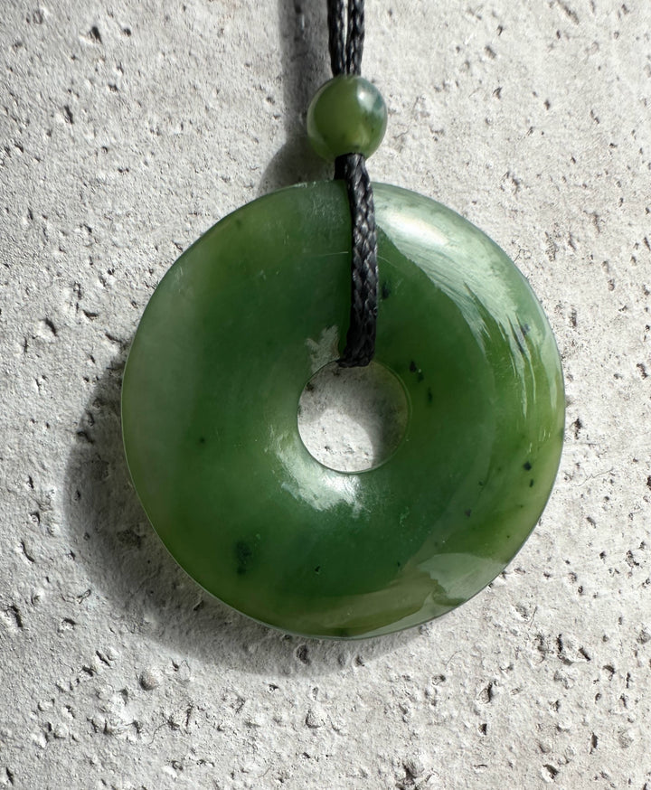 Green jade donut pendant with central hole on black cord and small bead above.