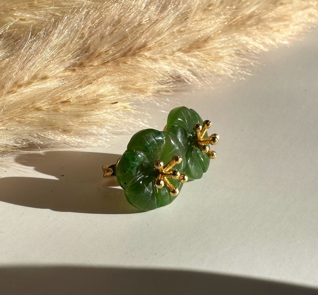 Jade flower earring with green circular petals and gold stamen accents on a light surface