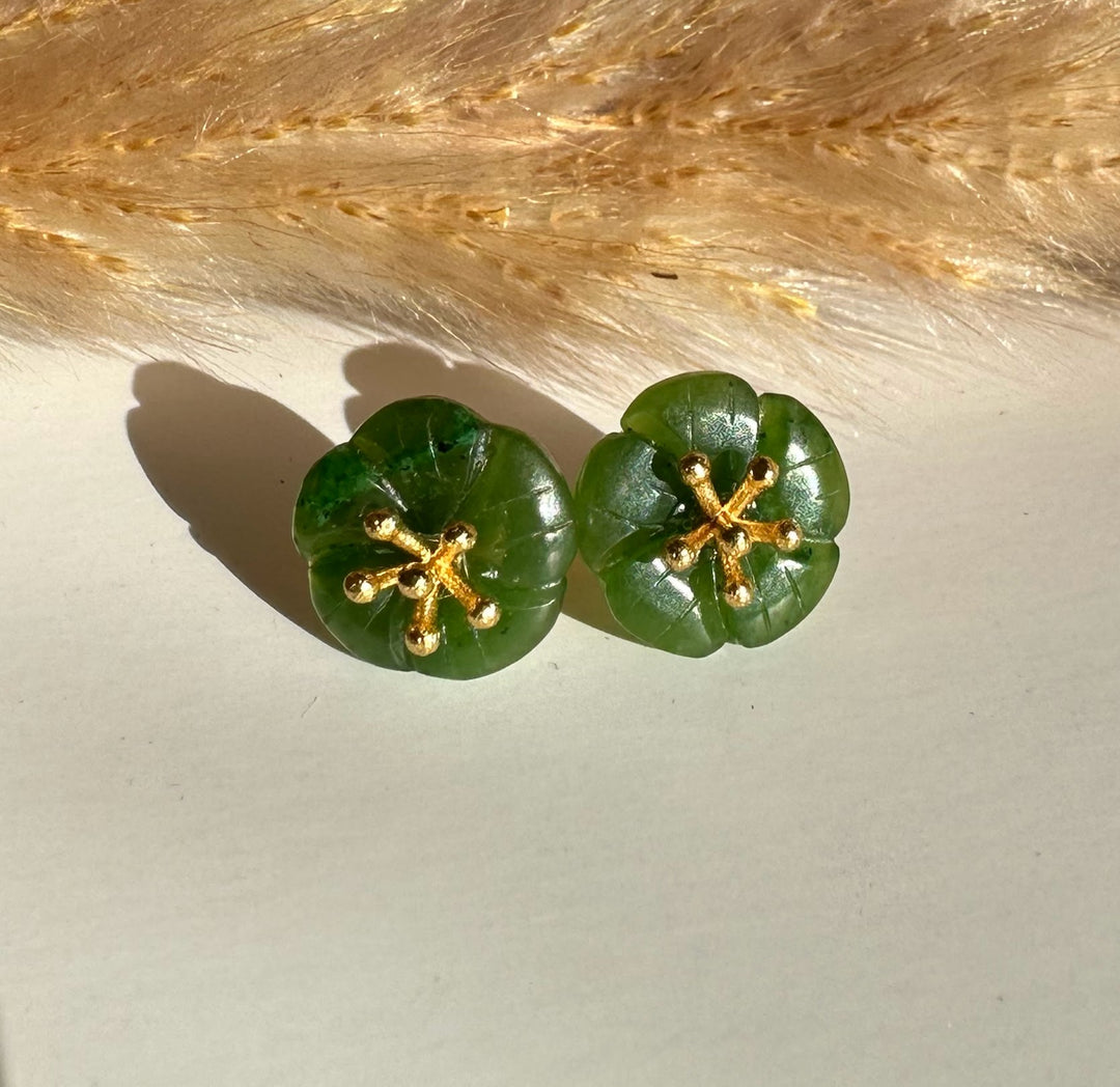 Pair of jade flower earrings with green petals and gold posts placed on a wooden table