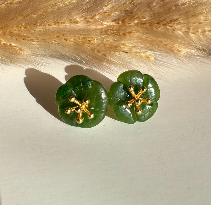 Pair of jade flower earrings with green petals and gold posts placed on a wooden table