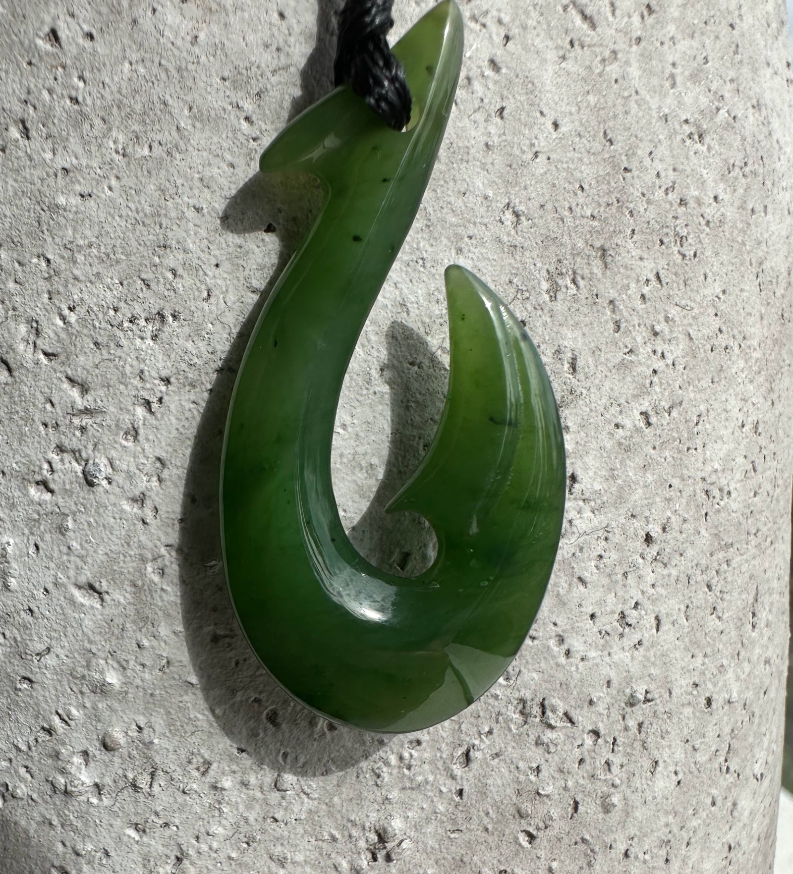 Green jade fish hook pendant with a curved hook design on a black cord