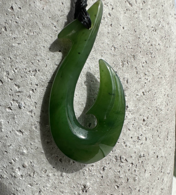 Green jade fish hook pendant with a curved hook design on a black cord