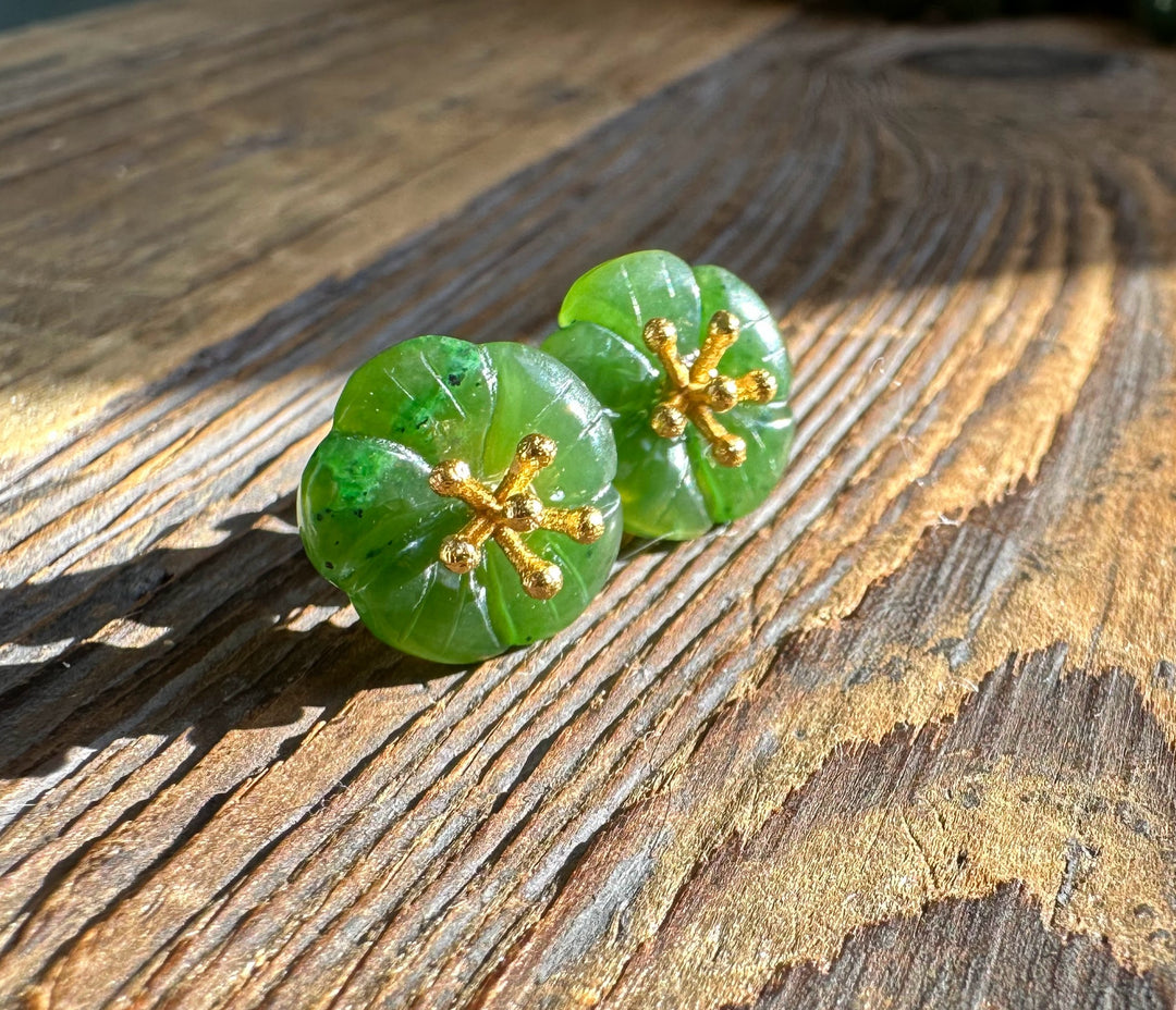 Green jade flower earrings with gold stamen centers on a rustic wooden surface.