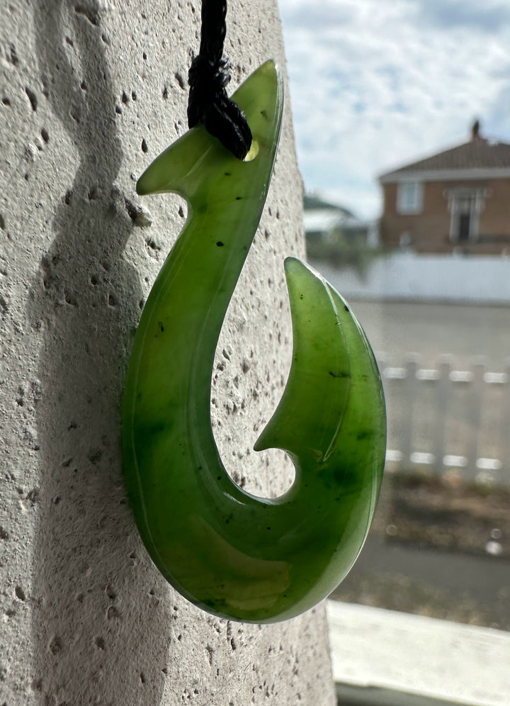 Glossy lime green fish hook pendant on a black cord against a textured concrete surface.