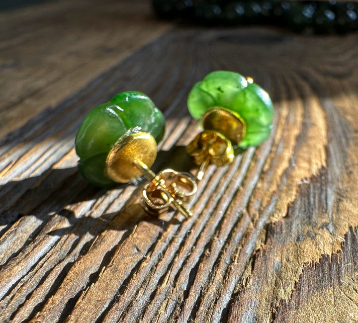 Close-up of jade flower earrings showing green petals and gold posts on a weathered wood surface