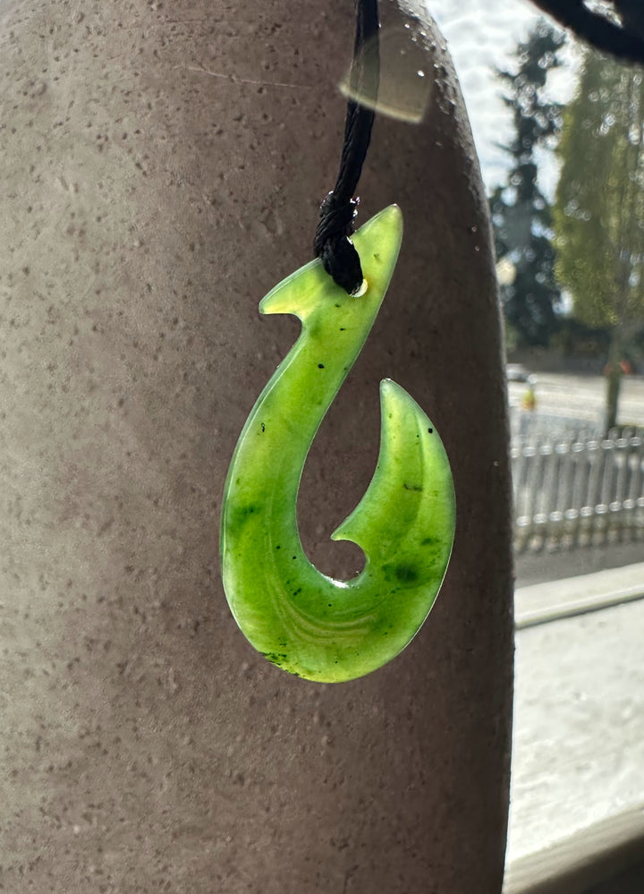 Bright green fish hook pendant with a black cord, outdoors against a textured wall.