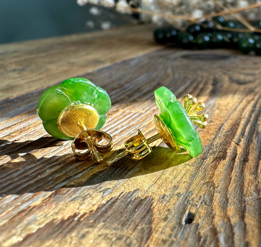 Green jade flower earrings with gold petals resting on a weathered wooden surface