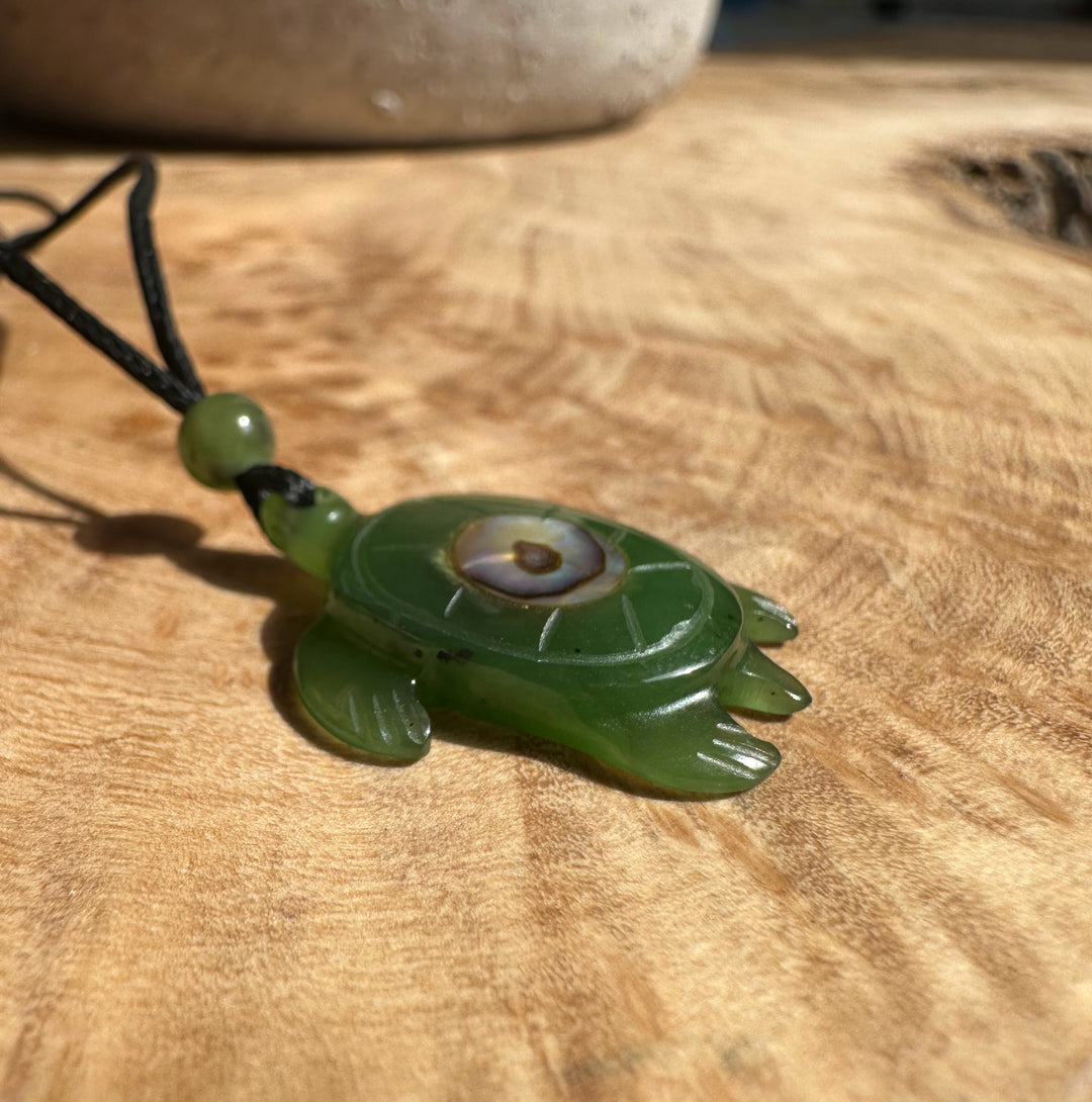 Green jade turtle pendant with abalone eye on a black cord resting on a wooden surface