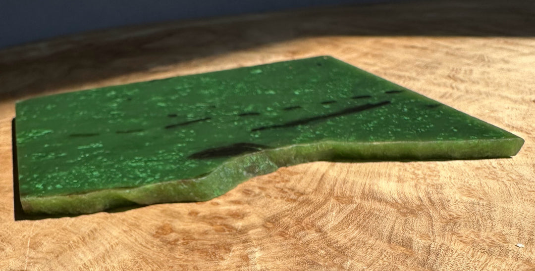 Close view of A Grade Canadian Cassiar Jade Slab showing emerald green surface on wood