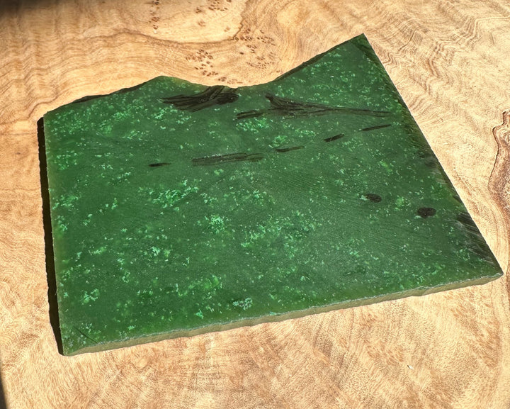 Angled shot of A Grade Canadian Cassiar Jade Slab with dark inclusions resting on wood board