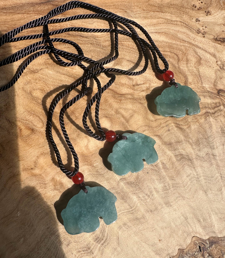 Guatemalan jadeite elephant pendants on black braided cords with red beads laid on a wooden surface