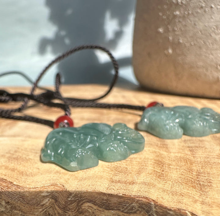 Two jadeite elephant pendants on black cords with red beads resting on a wooden surface