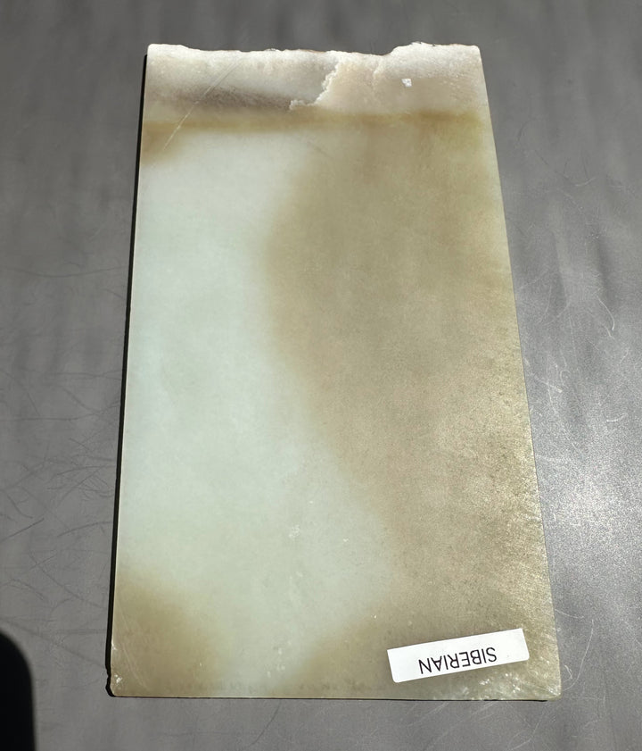 Honey white nephrite jade slab with subtle beige shading on a gray surface.