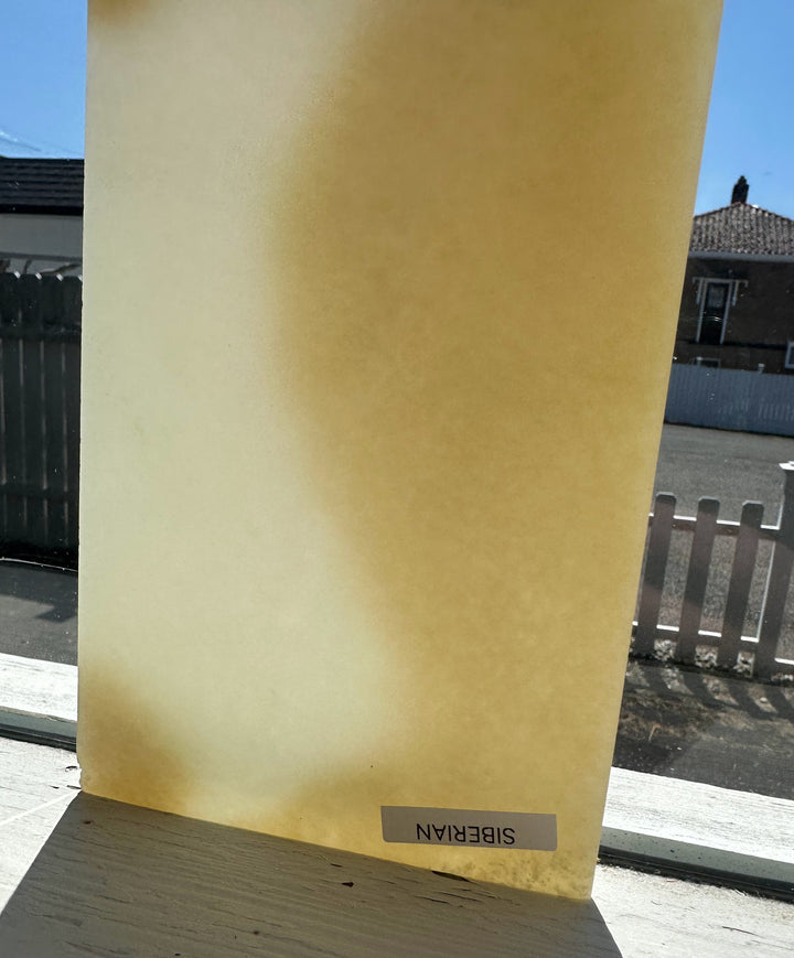 Honey colored nephrite jade slab outdoors with a pale gradient and a blue sky in the background