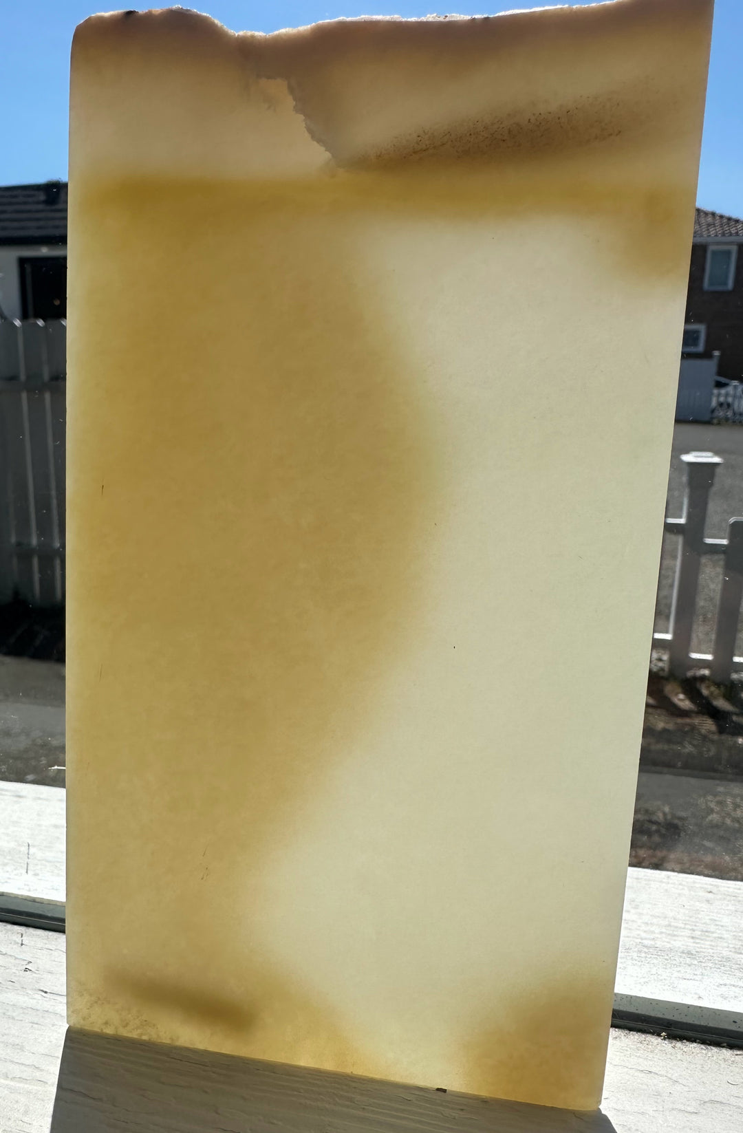 Honey white nephrite jade slab with warm yellow gradient and rounded top edge outdoors
