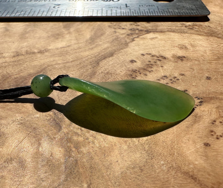 Green jade pendant on a wooden surface with a ruler for scale.