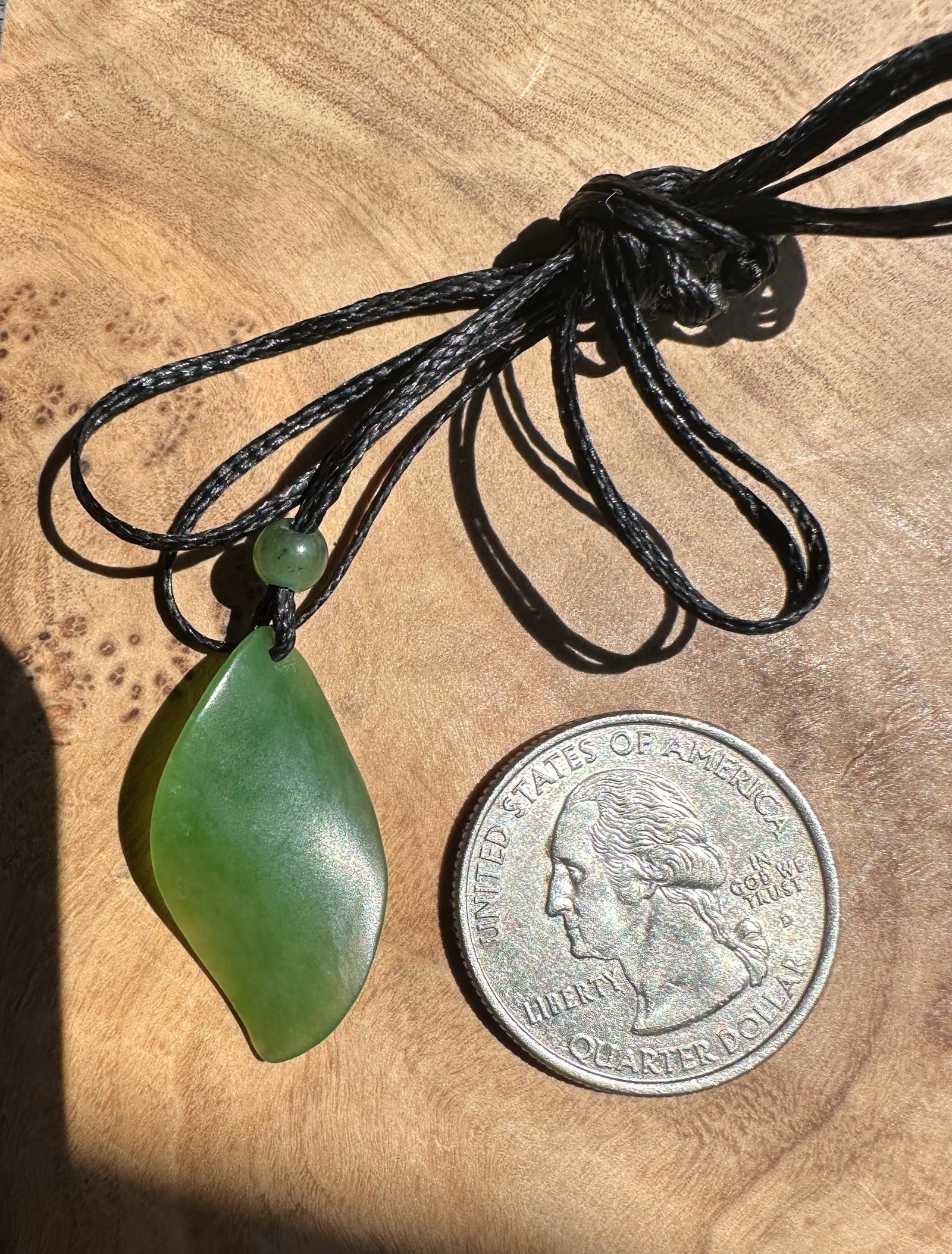 Green pendant on a black cord next to a quarter on a wooden surface