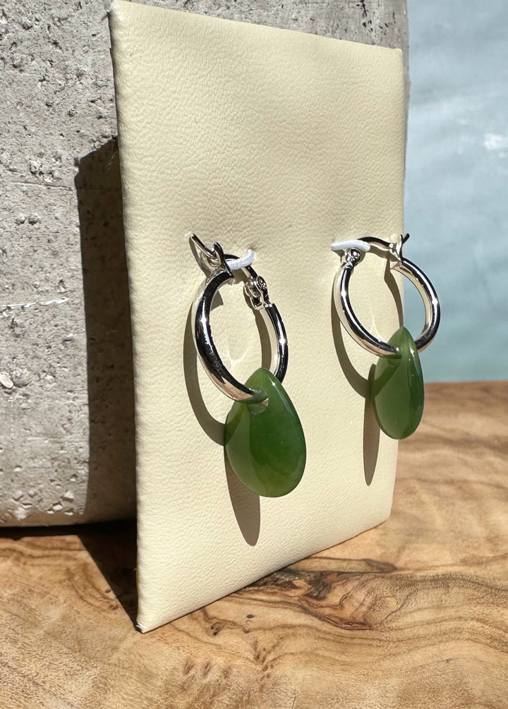 Green jade teardrop earrings with polished silver hoops displayed on a cream stand