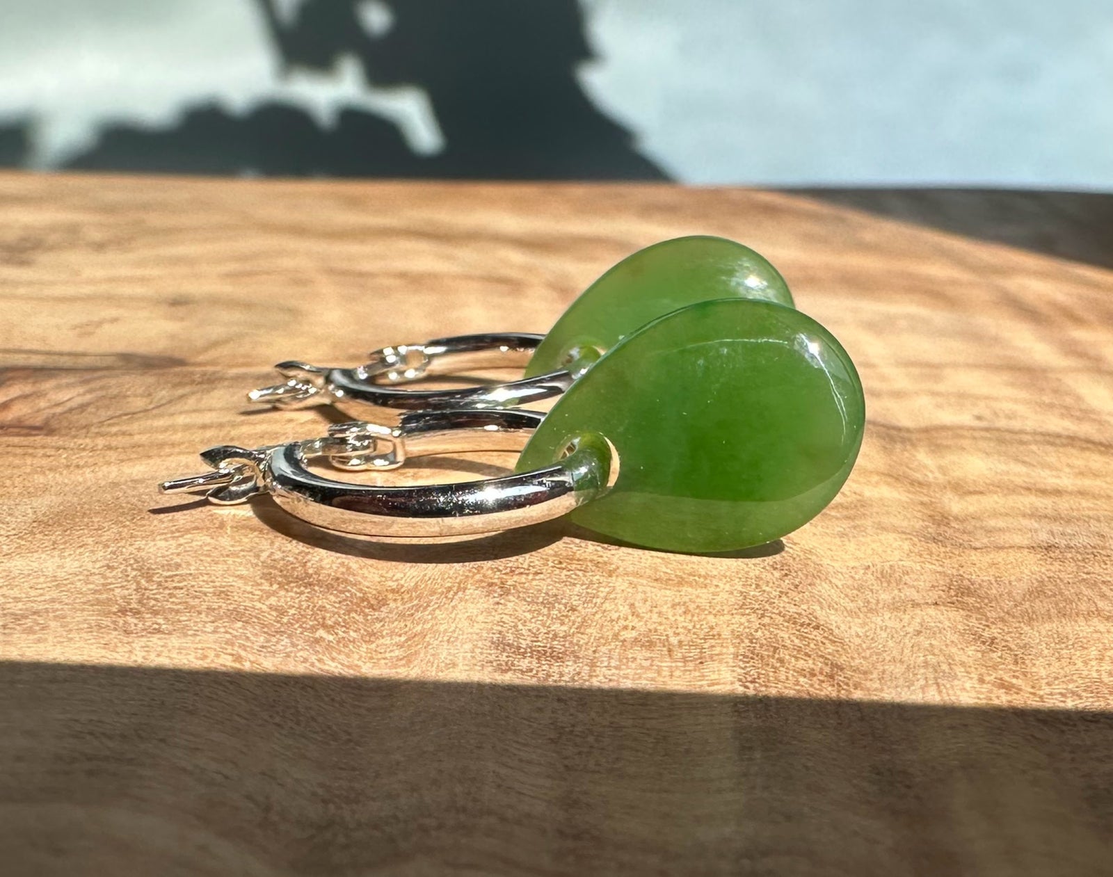 Pair of green jade teardrop earrings on silver hoops.