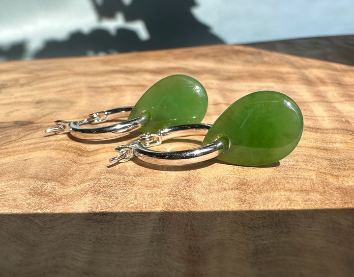 Close-up of jade teardrop earrings with silver hoops on a wooden surface