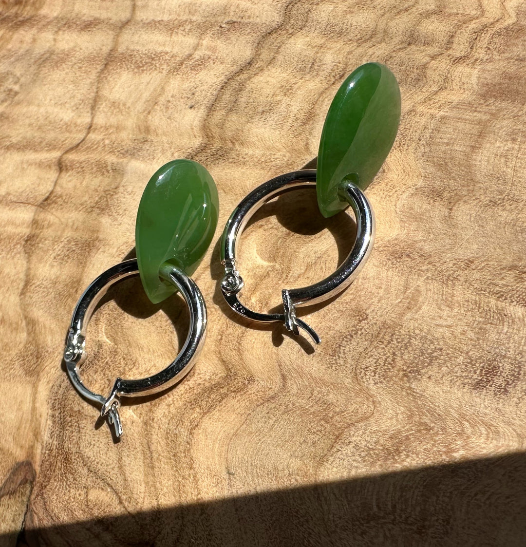 Side-angle view of jade teardrop earrings with silver hoops resting on a wood surface