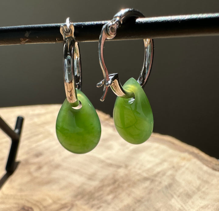 Green jade teardrop earrings with silver hoops hanging from a metal display