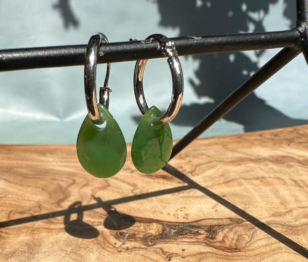 Pair of green jade teardrop earrings on silver hoops hung from a metal bar