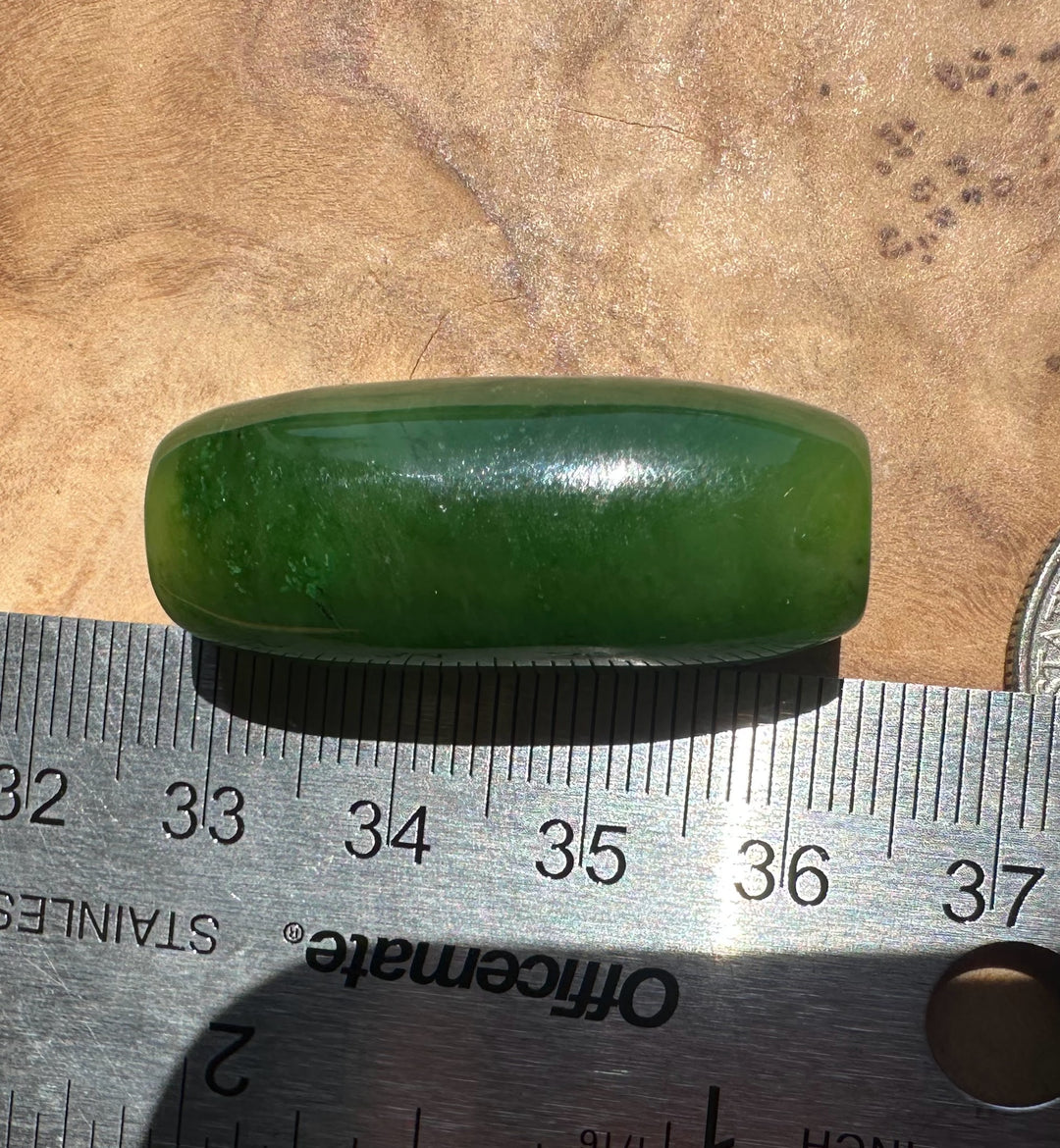 Green jade stone on a wooden surface with a ruler for scale.
