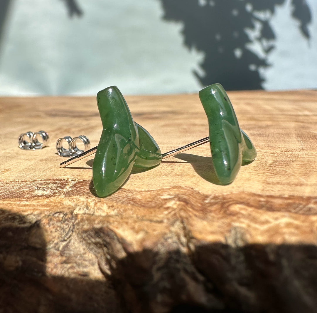 Jade whale tail stud earrings with metal posts and butterfly backs on a wooden surface.