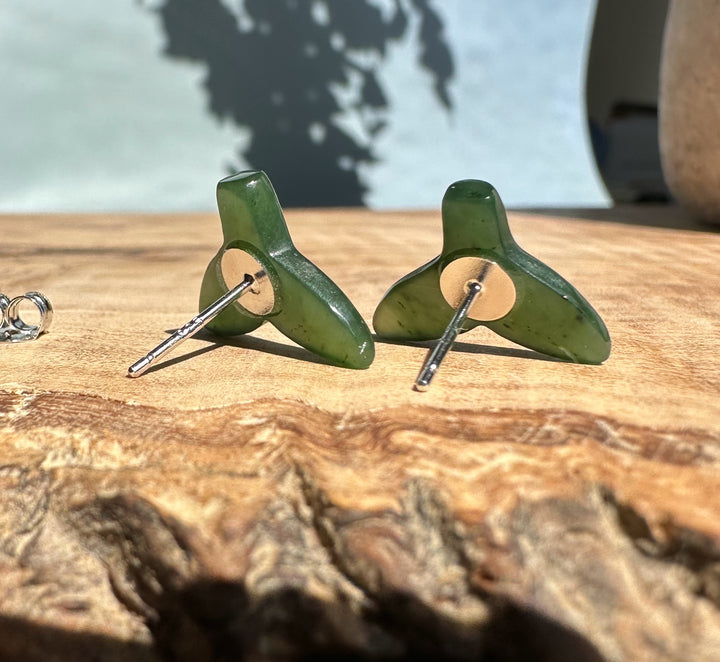 Jade whale tail studs shown from the back with posts and circular mounts on a wooden surface.