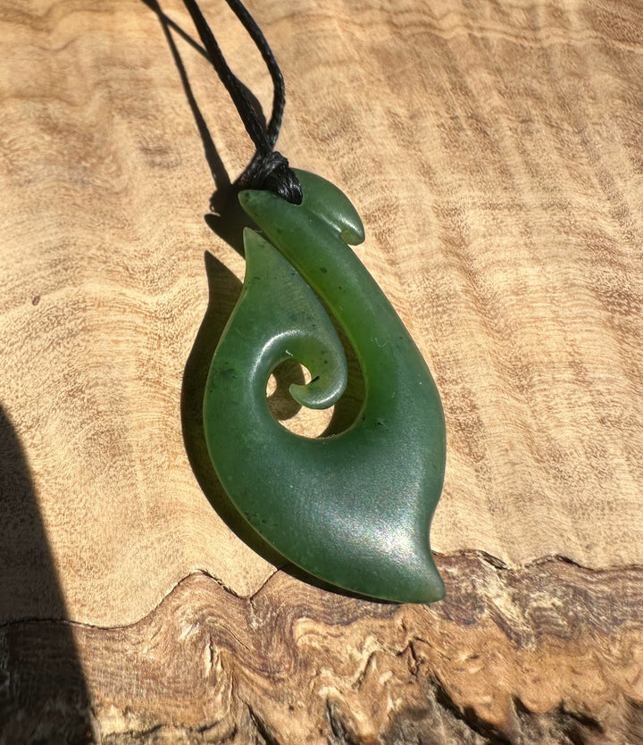 Green jade hook pendant on a wooden surface
