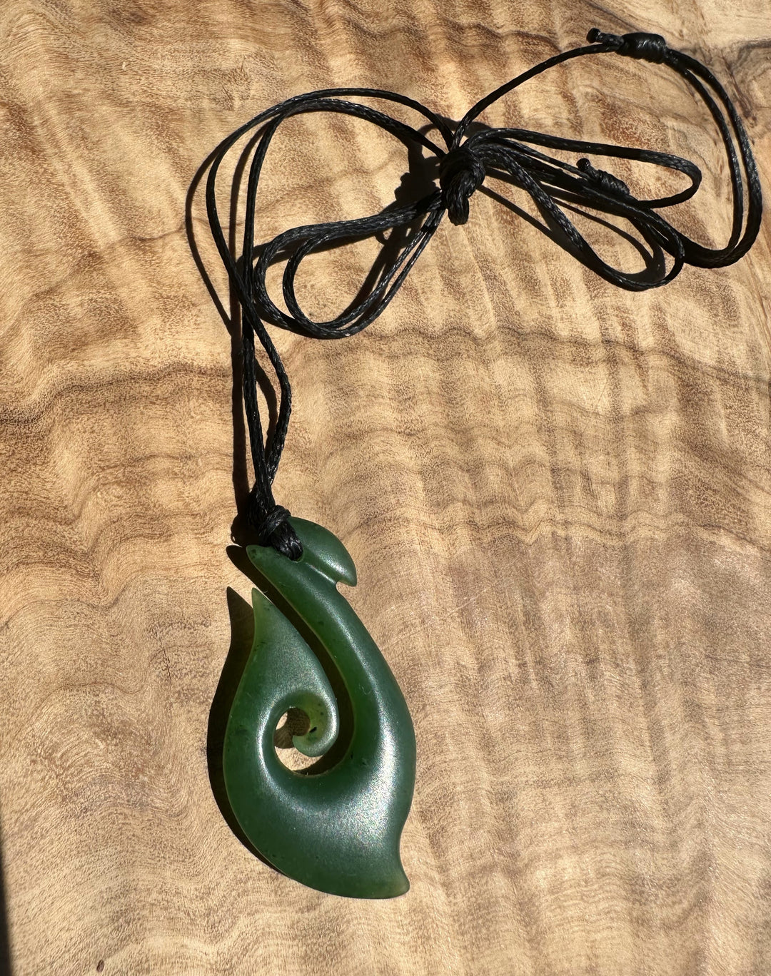 Green jade pendant on a black cord against a wooden background