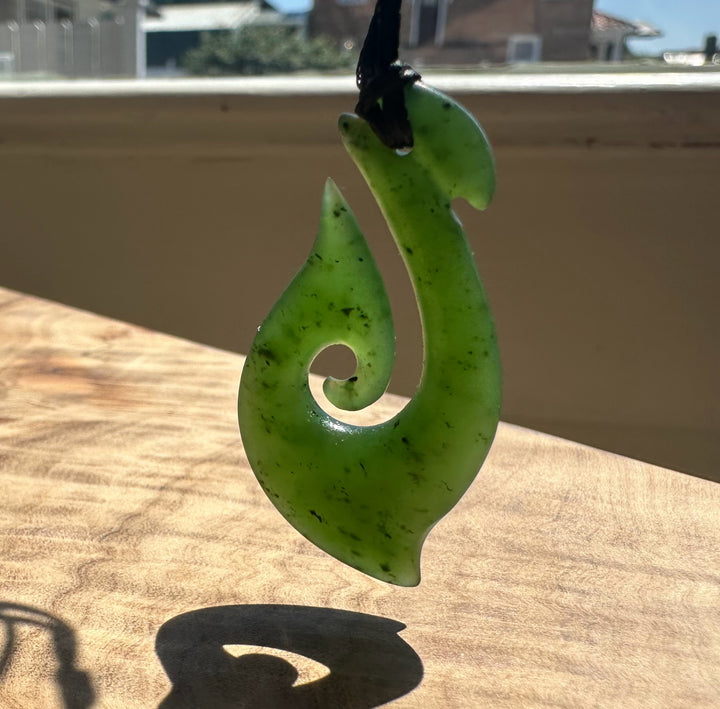 Green jade hook pendant on a wooden surface with a blurred background