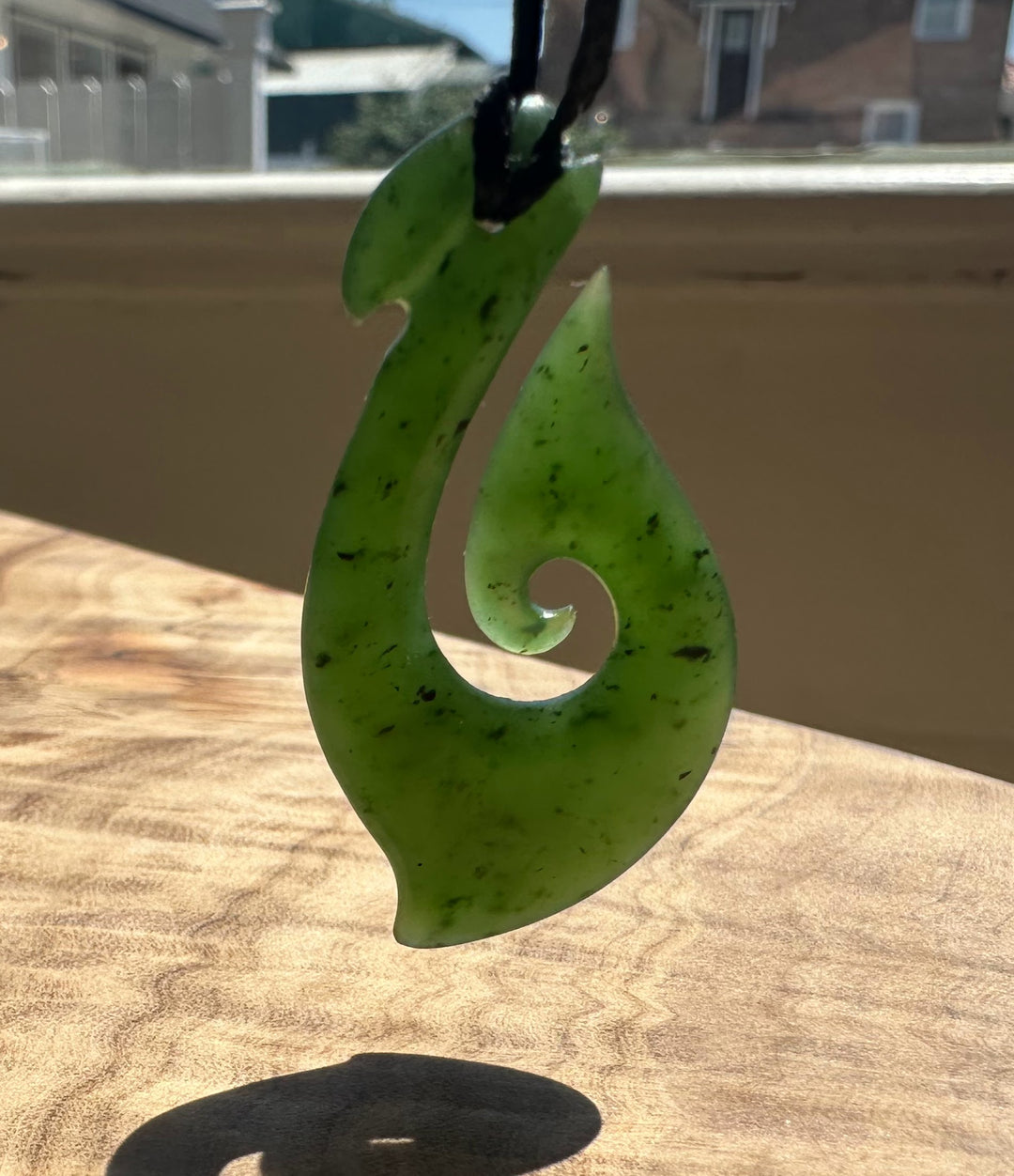 Green jade pendant on a wooden surface with a blurred outdoor background