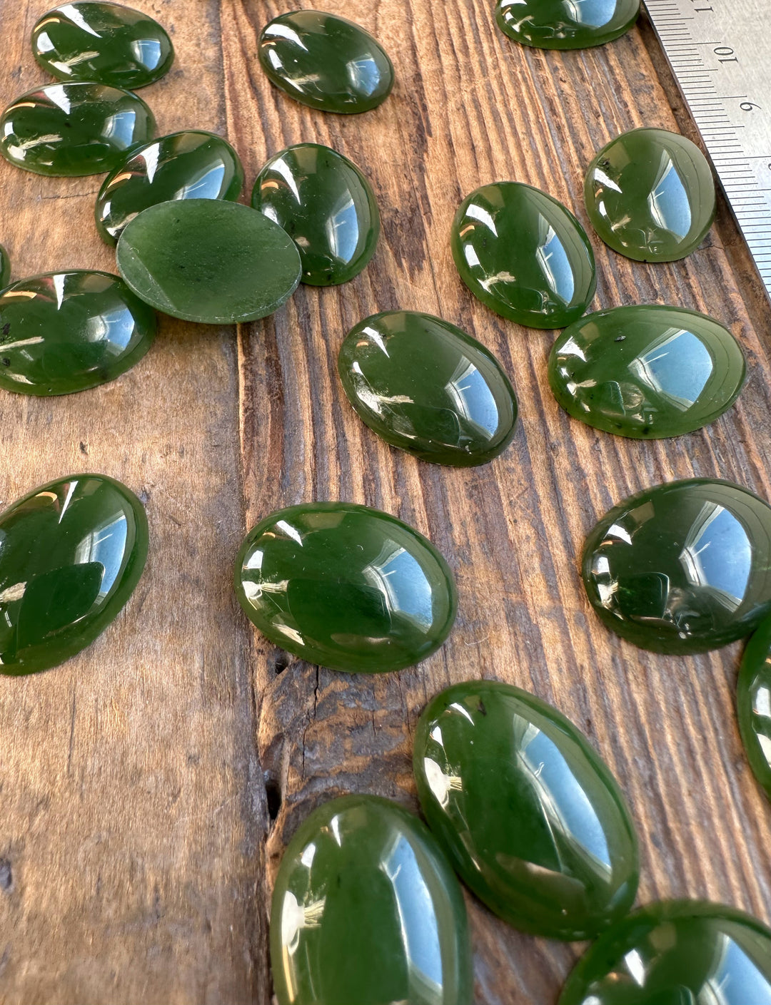 Group of polished Canadian nephrite jade oval cabochons on a rustic wood surface with a ruler for scale