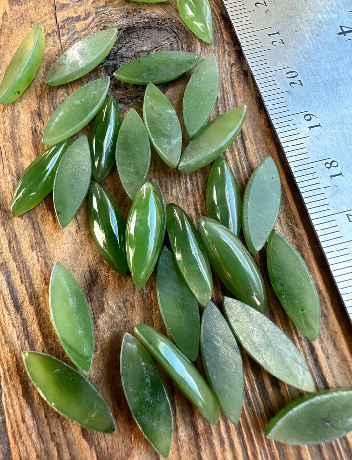 Assorted green marquise cabochons on wood with a ruler showing size