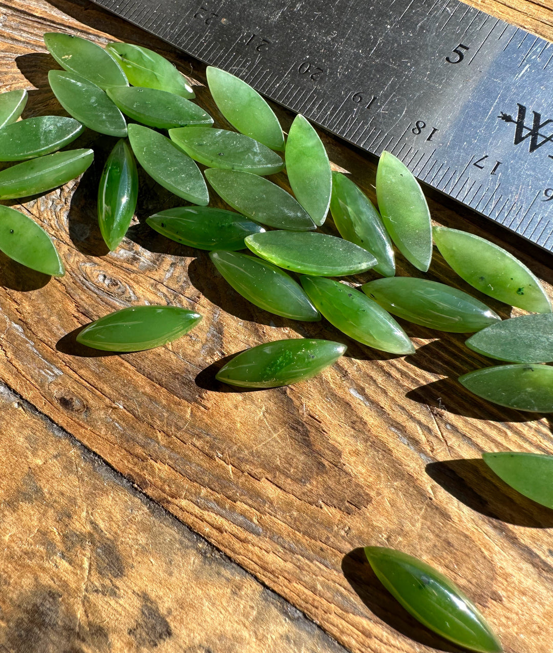 Green marquise cabochons scattered on a wooden surface beside a ruler for scale