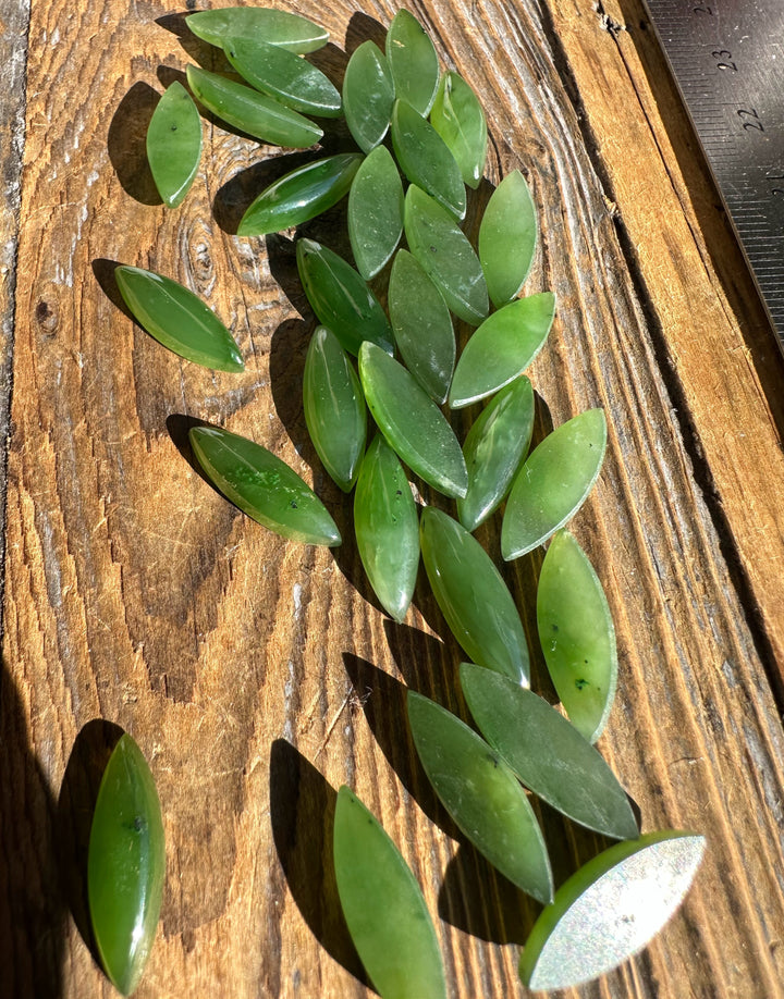 Cluster of green marquise cabochons on a wooden board with a ruler visible.